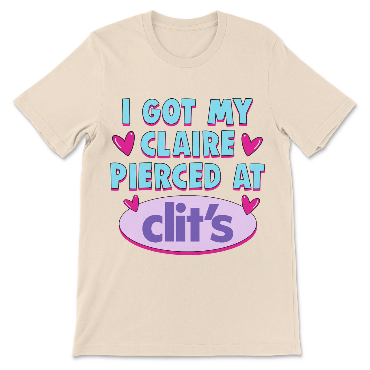 A light beige crewneck t-shirt featuring a colorful graphic print on the front that reads 'I GOT MY CLAIRE PIERCED AT clit's' with pink hearts and a purple oval logo, displayed on a clean white background.