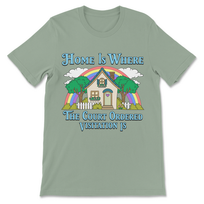 A sage green short-sleeve t-shirt with a colorful graphic of a house under a rainbow, accompanied by the text 'Home Is Where The Court Ordered Visitation Is'.