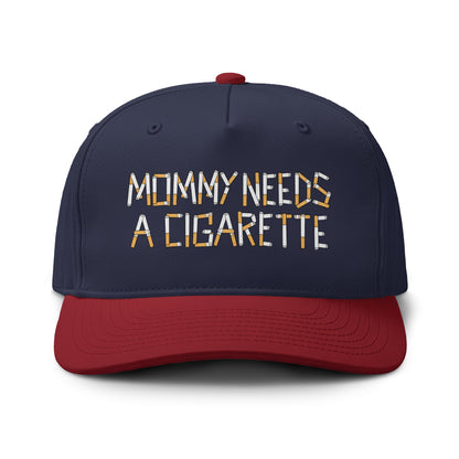 A navy blue and red baseball cap with the phrase 'MOMMY NEEDS A CIGARETTE' embroidered on the front. The letters in the text are filled with a cigarette pack pattern, and the cap has a red visor and matching red top button, shown against a plain white background.
