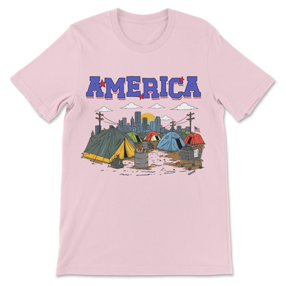 Funny America graphic tee depicting a homeless encampment with shopping carts and tents in a patriotic parody design.

