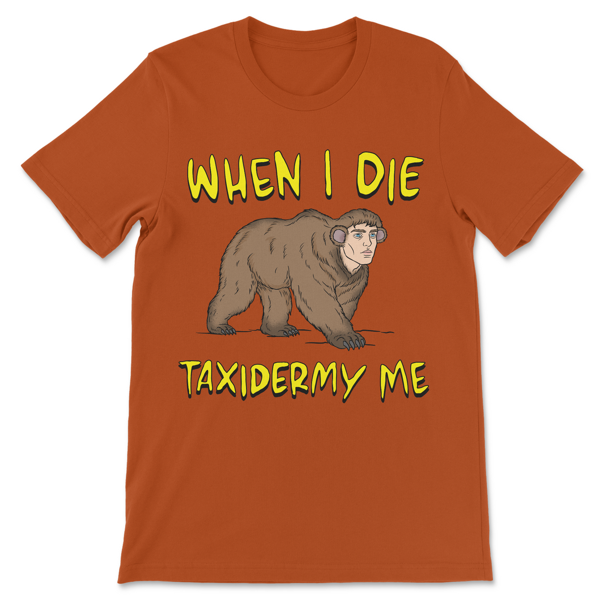 An orange crewneck t-shirt featuring a cartoon illustration of a brown bear wearing headphones, with the text 'WHEN I DIE' above and 'TAXIDERMY ME' below in a yellow font.